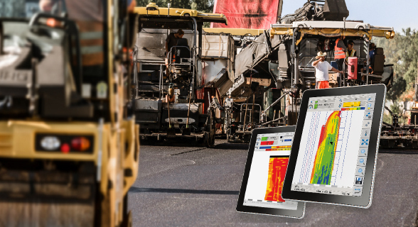 Vordergrund zeigt ein digitales Messgerät auf einem Tablet mit detaillierter farbiger Grafik, im unscharfen Hintergrund ist eine große Asphaltiermaschine mit Arbeitern auf einer Baustelle zu erkennen.